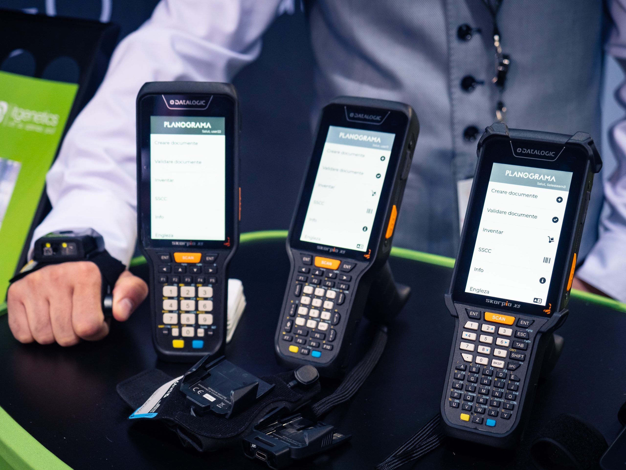 Drei Handheld-Computer von Datalogic mit der Planograma-App auf dem Tresen des Stands, daneben ein Barcode-Scanner, den ein Teammitglied an der Hand trägt
